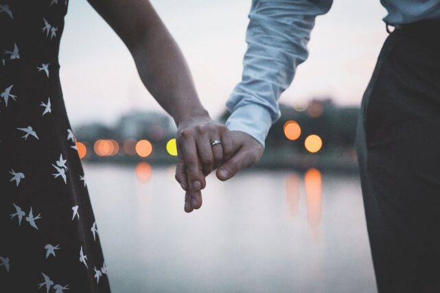 Close-up photo of man and woman holding hands with woman's ring as focal point hoping to get visa and green card